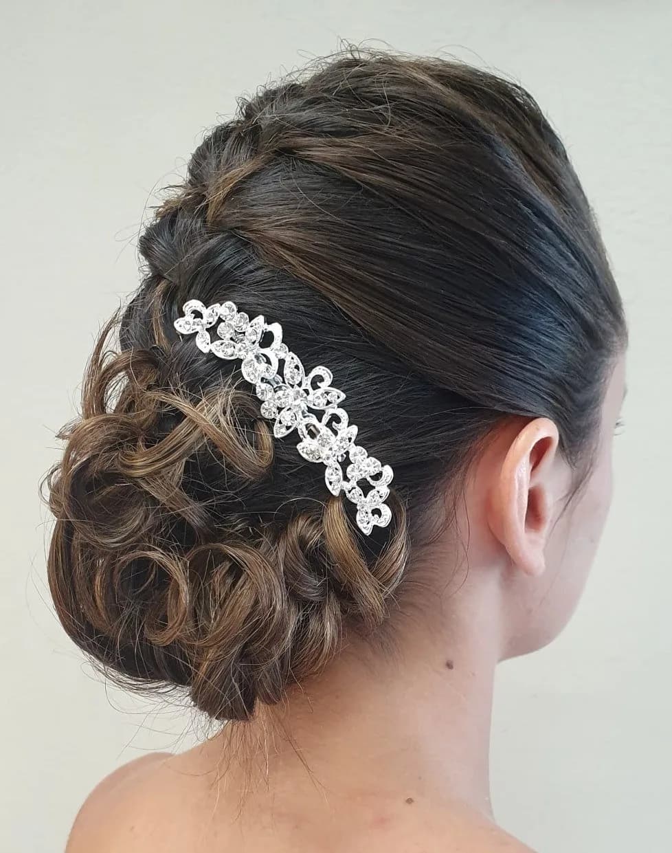 Chignon bas bouclé sur cheveux châtain foncé, vu de dos, retenu par un peigne bijou argenté