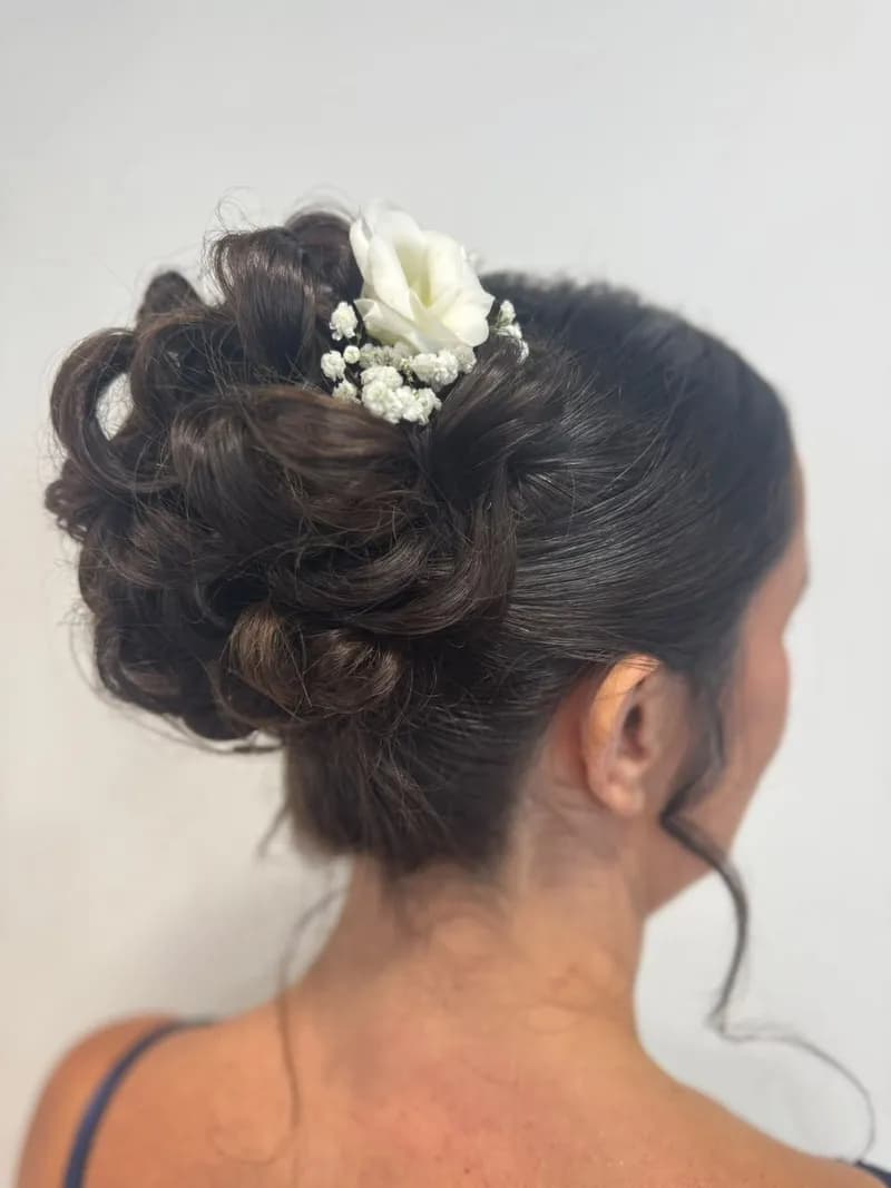 Chignon bouclé sur cheveux bruns, vu de trois quarts dos, piqué d'une fleur blanche et de gypsophile