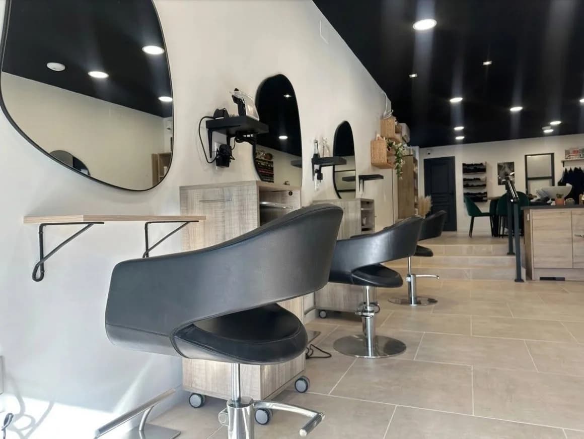 Le salon Innecto : fauteuils noirs alignés face à des miroirs arrondis, meubles en bois clair et plafond noir à spots