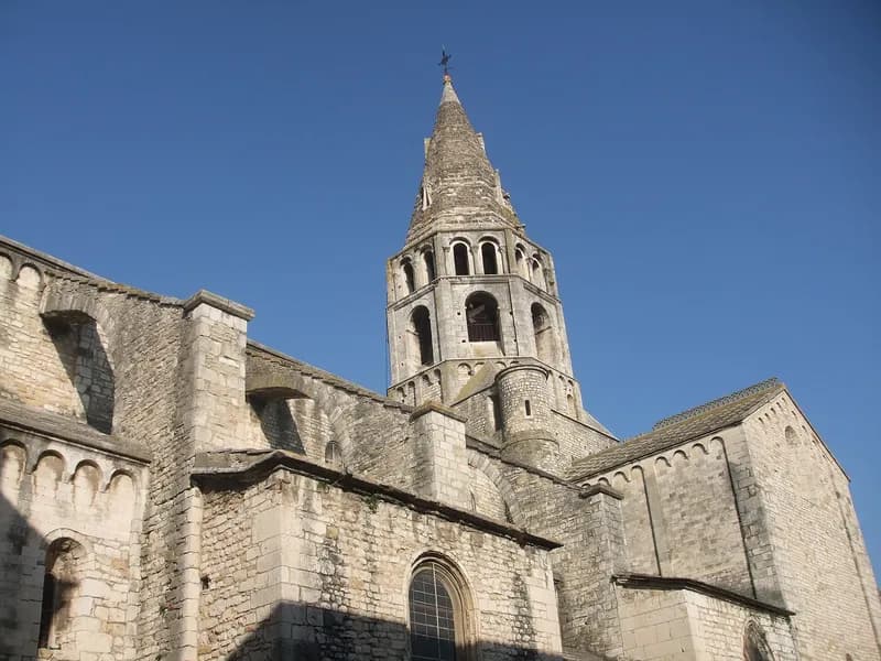 L'église Saint-Andéol vue de l'extérieur : murs de pierre claire et clocher roman à flèche, sous un ciel bleu