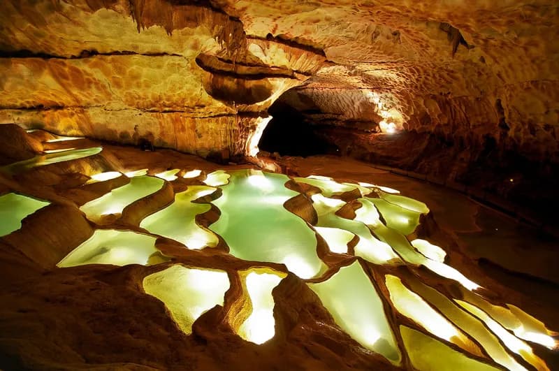 La cascade de gours de la grotte de Saint-Marcel : des bassins en gradins éclairés en vert et or dans une galerie